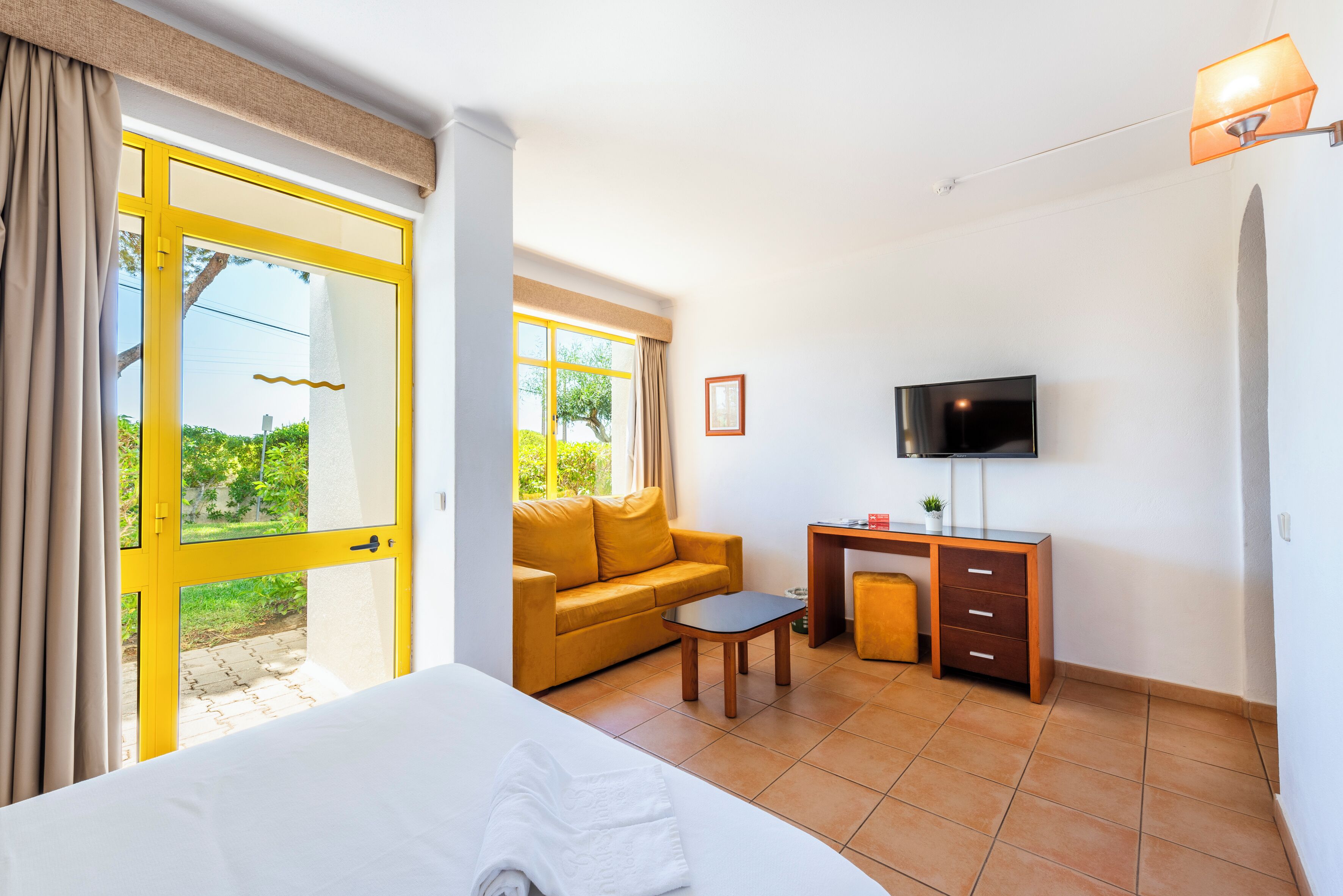A hotel room with a bed, a sofa, a desk, a TV, and a window with curtains.
