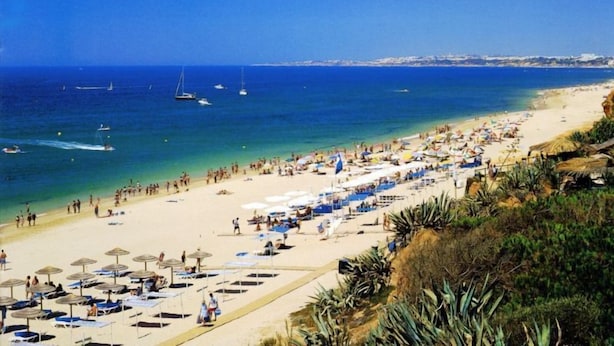 A beach with sun loungers and umbrellas, a clear blue sea, and boats in the distance. - Hotel Pinhal do Sol (Loulé)