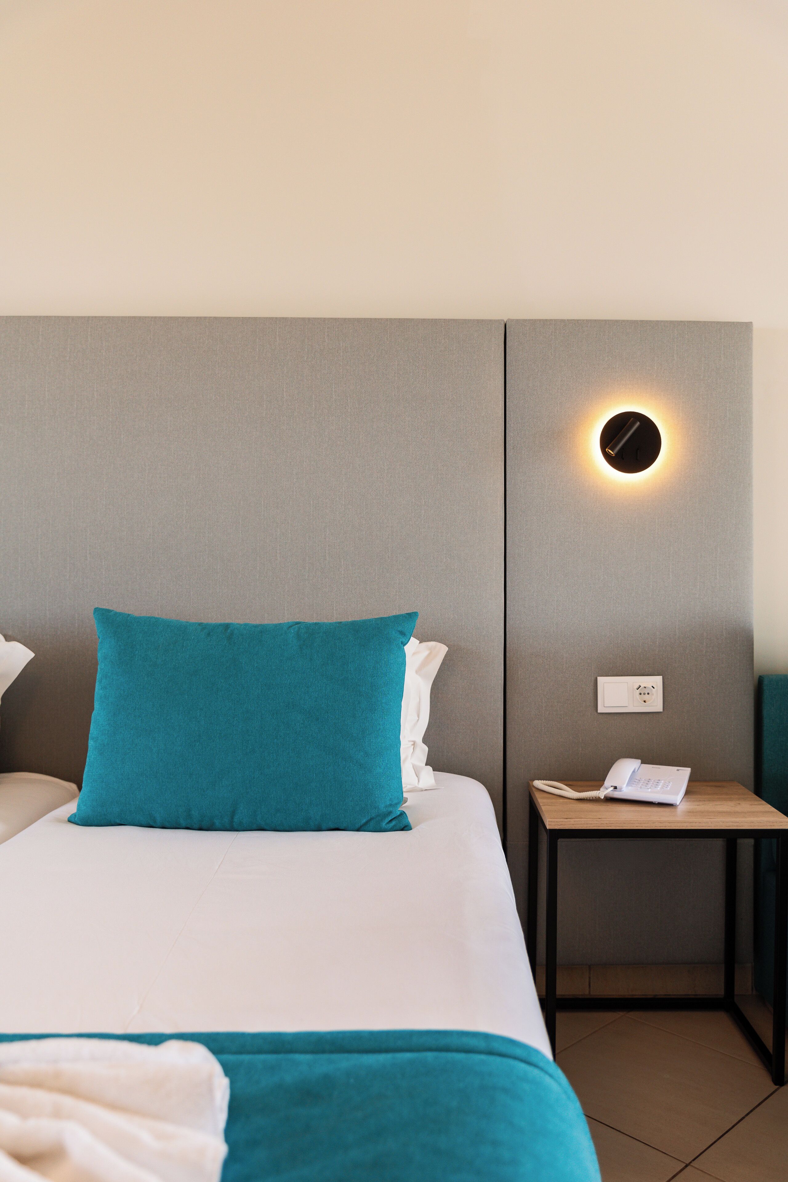 A hotel room with a bed, a nightstand, a lamp, and a wall-mounted light fixture.