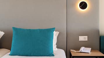 A hotel room with a bed, a nightstand, a lamp, and a wall-mounted light fixture.