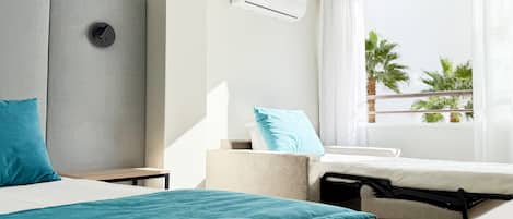 Habitación de hotel con cama, una silla, una mesita, aire acondicionado y ventana con vista a palmeras.