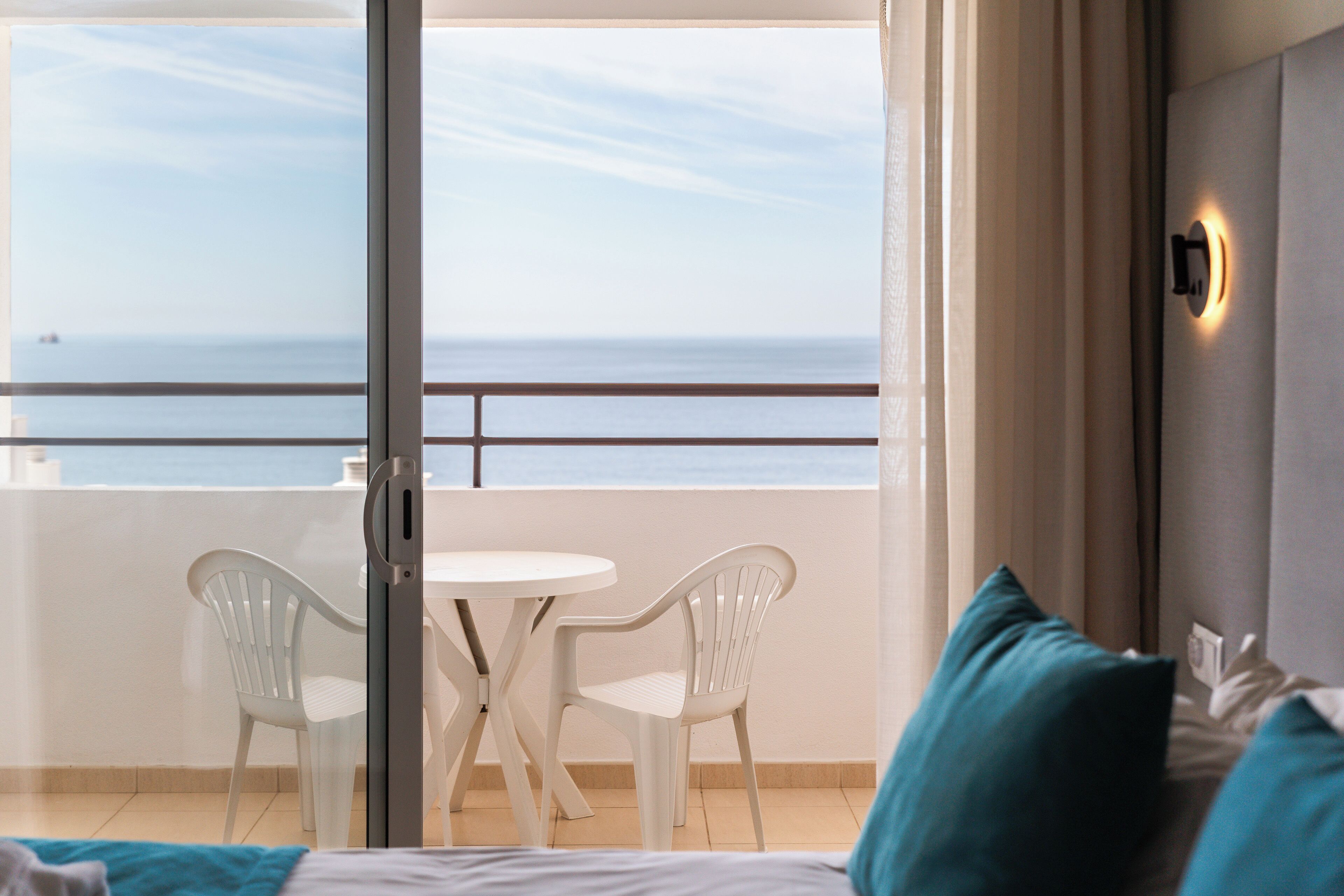A hotel room with a balcony, a bed, a table, two chairs, and a view of the sea.