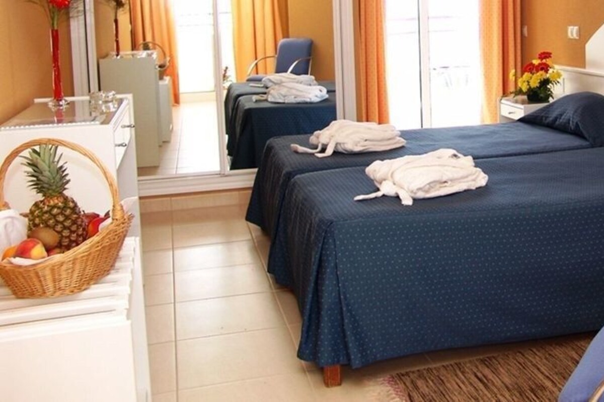 A hotel room with two beds, a desk with a telephone, a chair, and a small table with a basket of fruit.