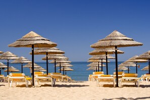 A beach with rows of sun loungers and thatched umbrellas. - Hotel Atismar (Loulé)