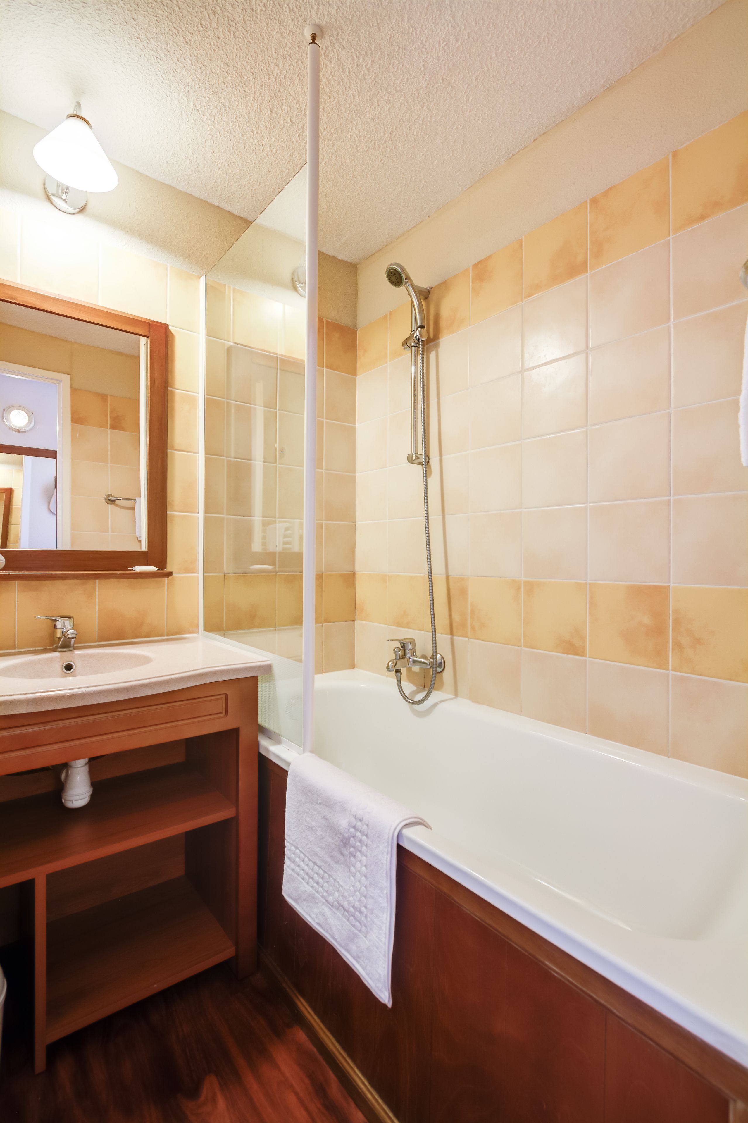A bathroom with a wooden vanity, a white sink, a mirror, and a bathtub with a showerhead.