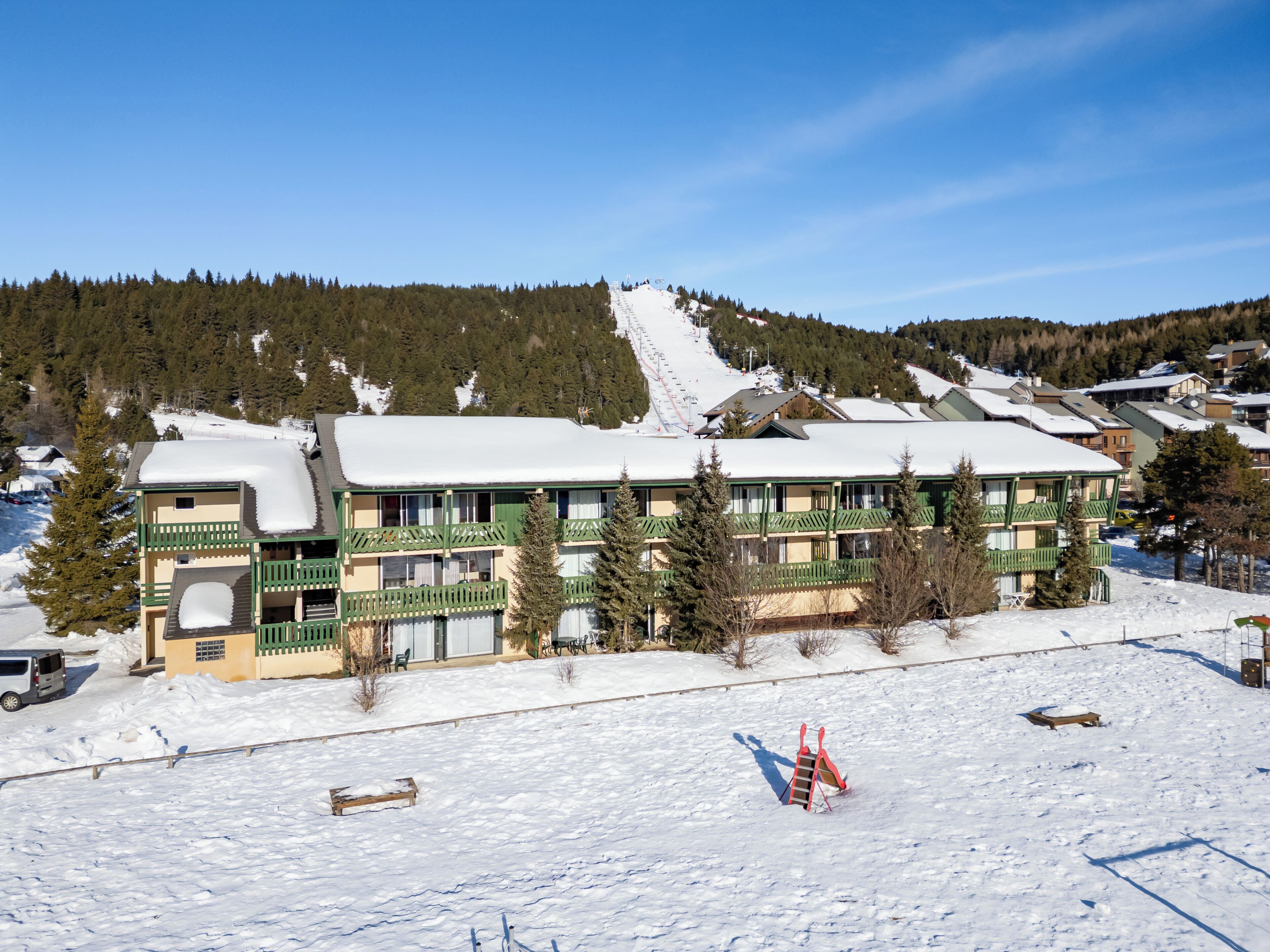 A hotel with multiple balconies, a ski slope in the background, and a snow-covered ground.