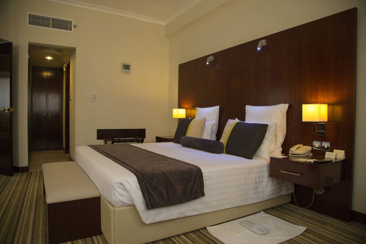 A hotel room with a large bed, bedside lamps, a nightstand, and a desk.