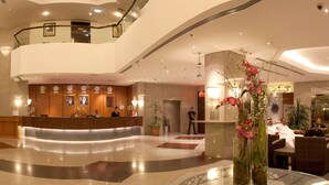 Rebedor d'hotel amb taulell de recepció, zona de seients i taula de vidre amb bocs de flors.