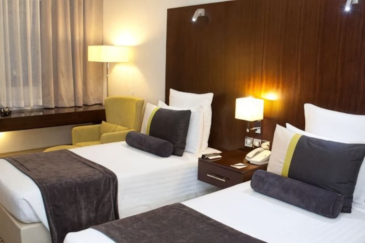 A hotel room with two beds, a desk, a chair, and a lamp.