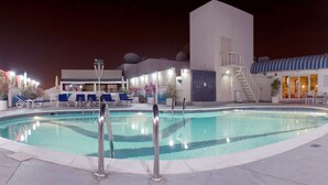 Una piscina amb gandules i un edifici de façana blanca amb detalls blaus.