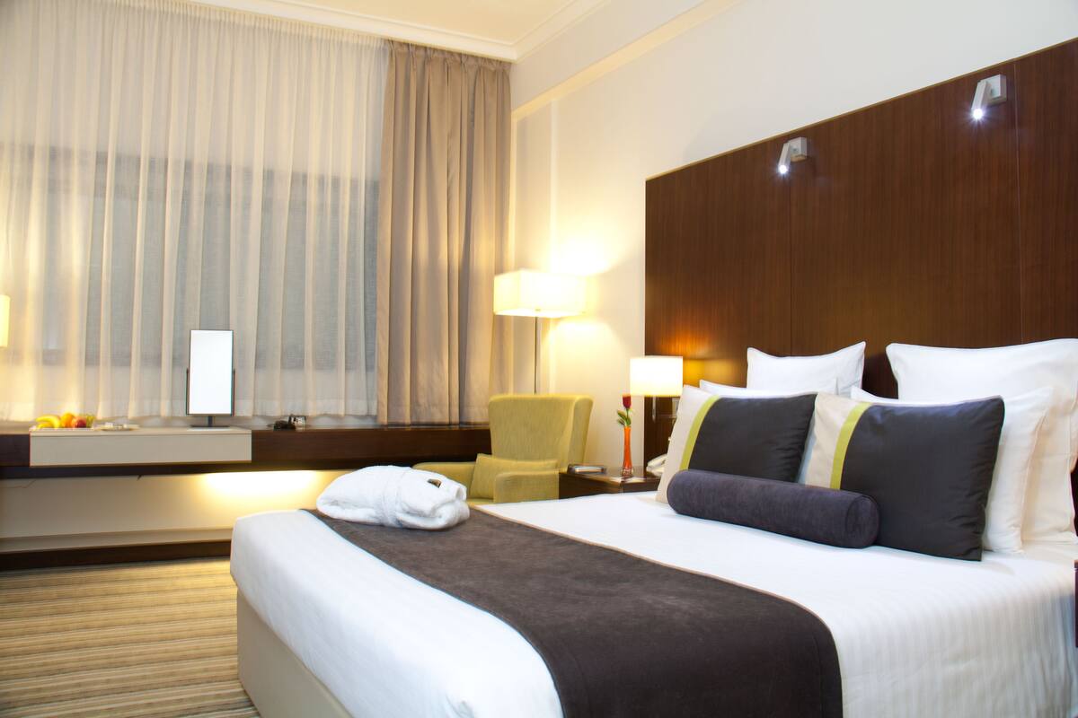 A hotel room with a large bed, a chair, a desk, and a window with curtains.