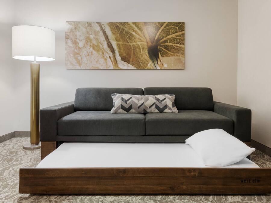 En moderne stue med en grå sofa, en sengegavl i træ, en gulvlampe og et marmorbillede på væggen.