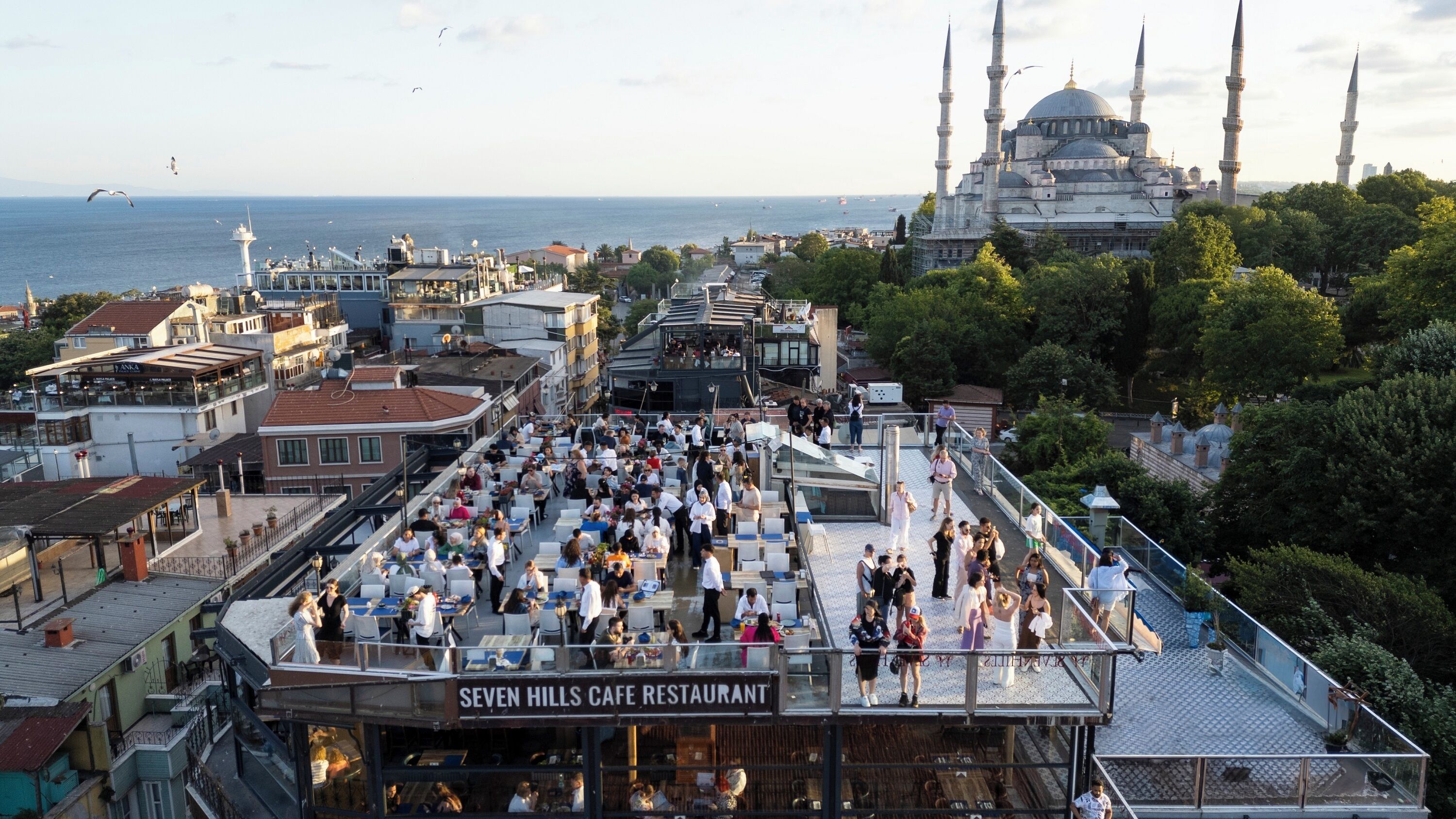 A rooftop café with outdoor seating, overlooking a cityscape and a mosque.