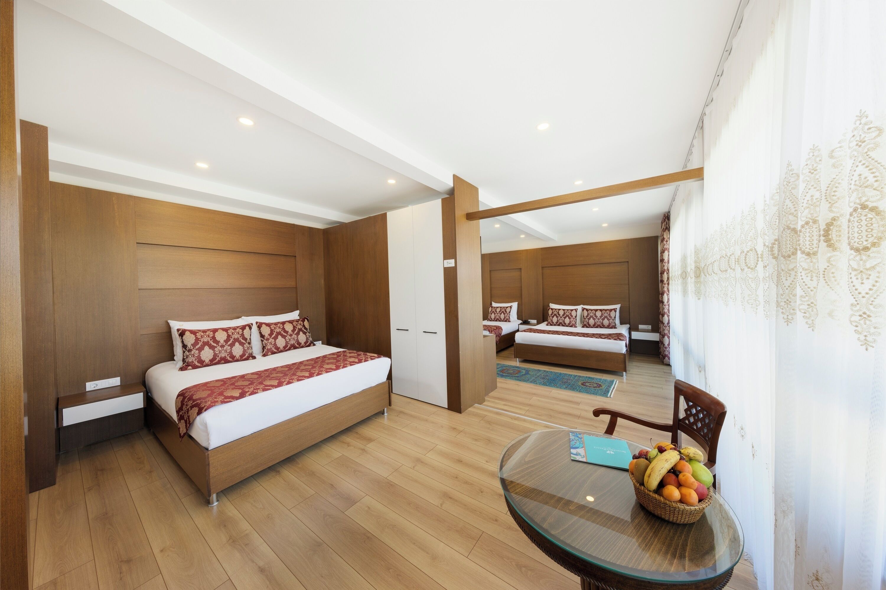 Una habitación de hotel moderna con una cama grande, una zona de estar separada y una mesa de comedor con fruta.