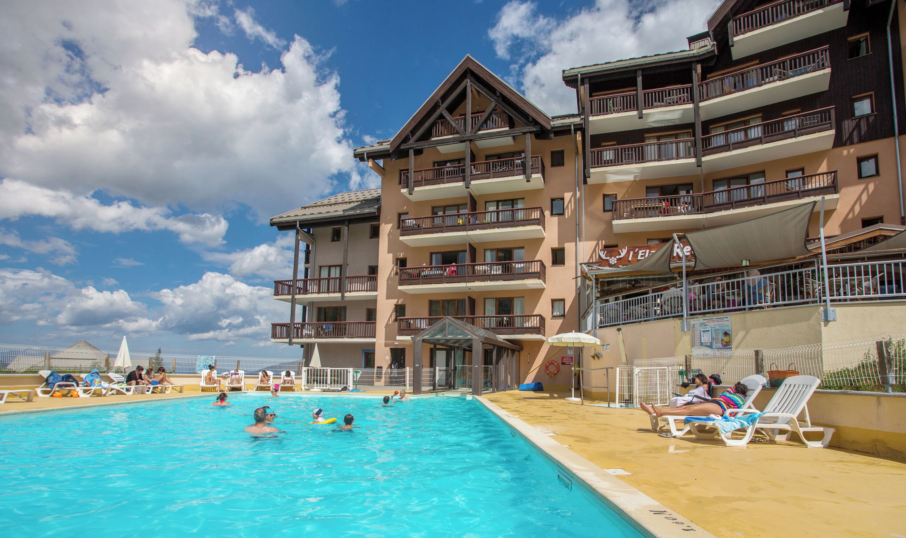 A hotel with a swimming pool, multiple balconies, and a clear sky.