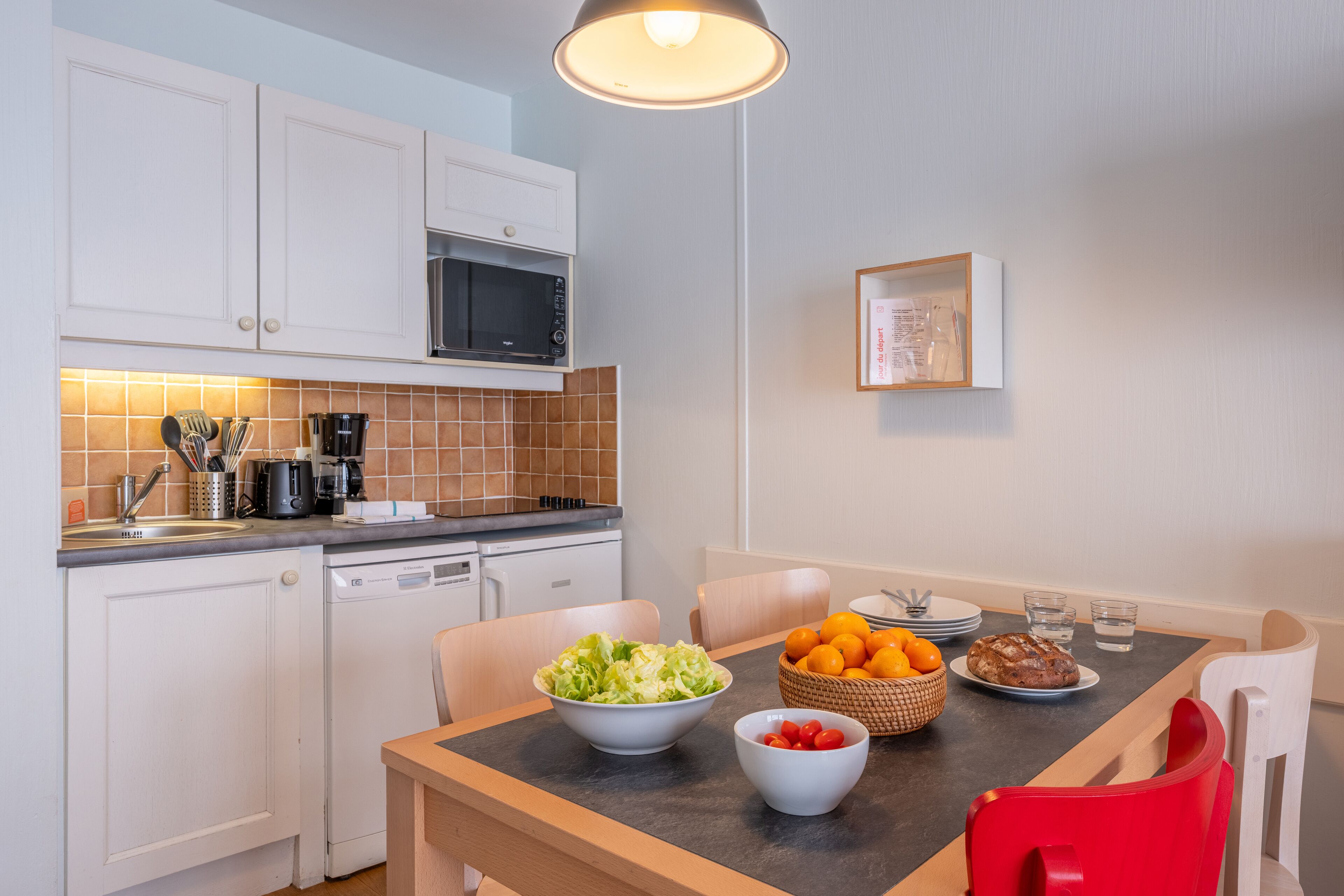 Una cocina moderna con armarios blancos, un microondas y un comedor con una mesa preparada para dos personas.