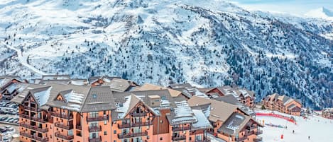 Un complejo turístico en la montaña cubierto de nieve, con edificios de varios pisos que incluyen balcones y pistas de esquí.
