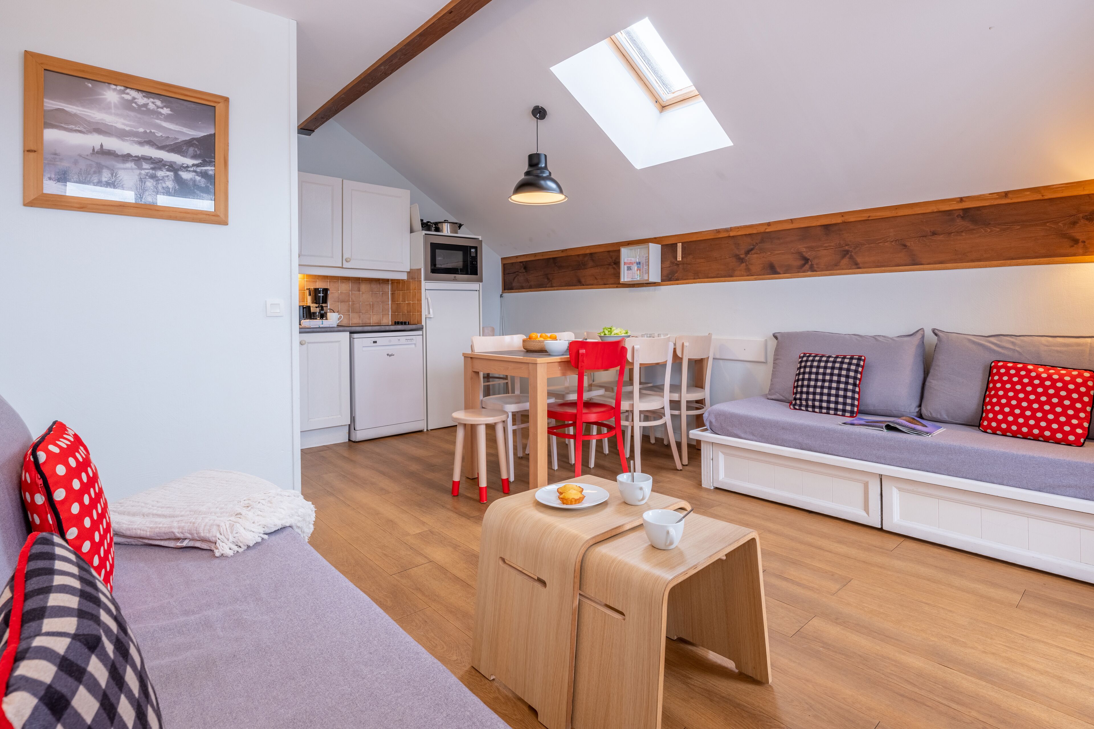 A compact living space with a kitchenette, a sofa with cushions, a dining area, and a skylight.
