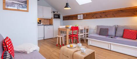 A compact living space with a kitchenette, a sofa with cushions, a dining area, and a skylight.