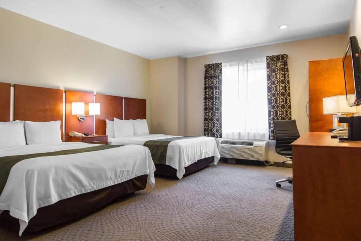 Ein Hotelzimmer mit zwei Betten, einem Schreibtisch, einem Stuhl, einem Telefon, einer Lampe und einem fenster mit Vorhängen.
