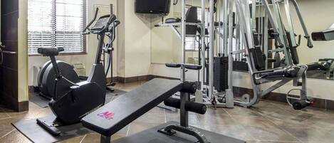 Uma academia com equipamentos de ginástica, um banco de musculação e uma esteira.