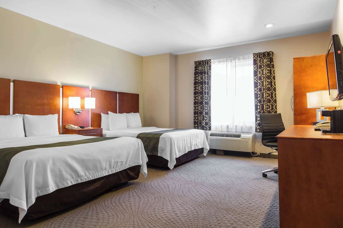 Ein Hotelzimmer mit zwei Betten, einem Schreibtisch, einem Stuhl, einem Telefon und einem Vorhangfenster.