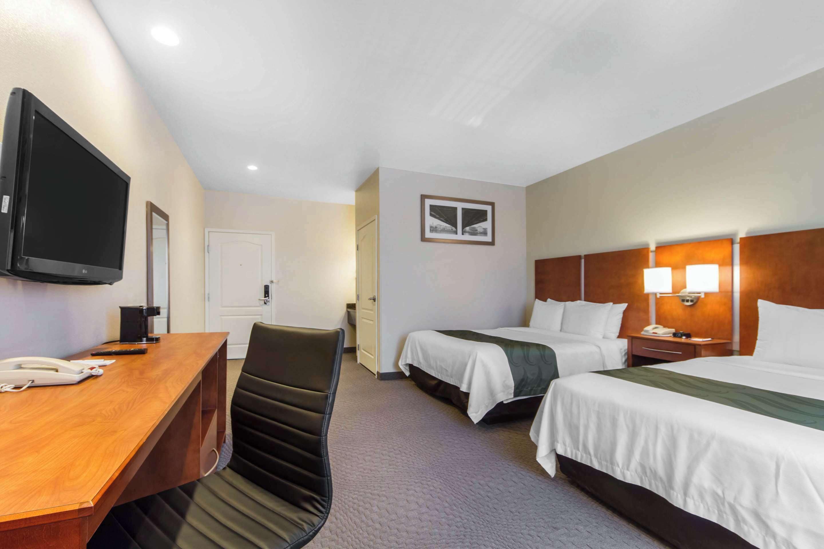 Une chambre d’hôtel avec un bureau en bois, deux lits, une télévision et une porte.