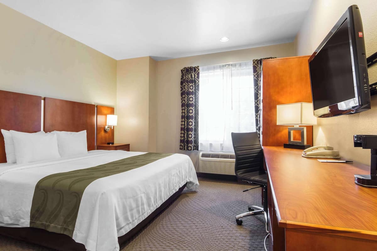 Ein Hotelzimmer mit einem großen Bett, einem Schreibtisch mit Stuhl, einem Fernseher und einem Fenster mit Vorhängen.