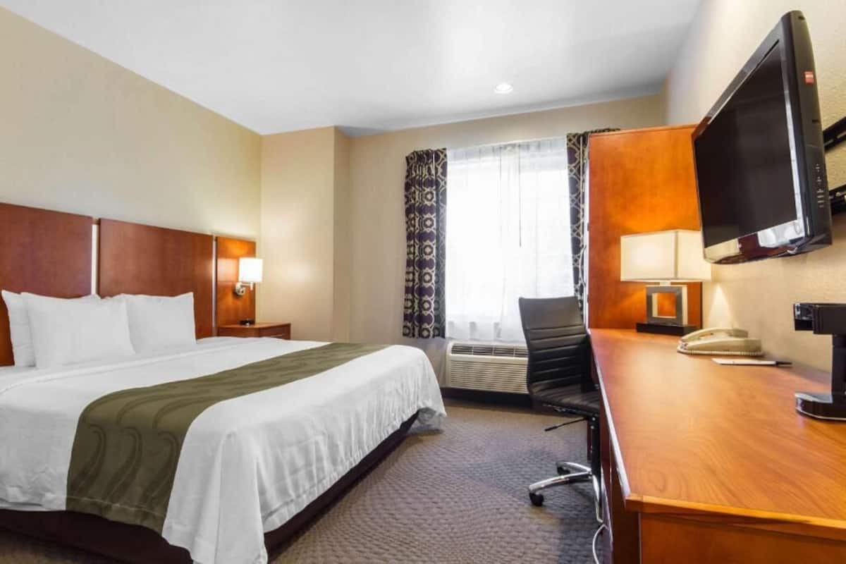 Ein Hotelzimmer mit Bett, Schreibtisch, Stuhl, Fernseher und einem Fenster mit Vorhängen.