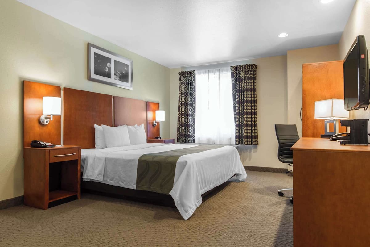 Ein Hotelzimmer mit Bett, Nachttischen, Schreibtisch, Stuhl, Fernseher und einem Fenster mit Vorhängen.
