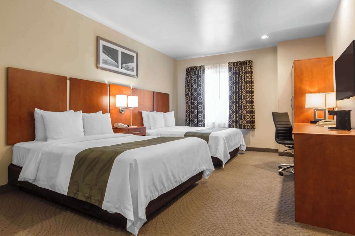 Ein Hotelzimmer mit zwei Betten, einem Schreibtisch, einem Stuhl und einem Fernseher.