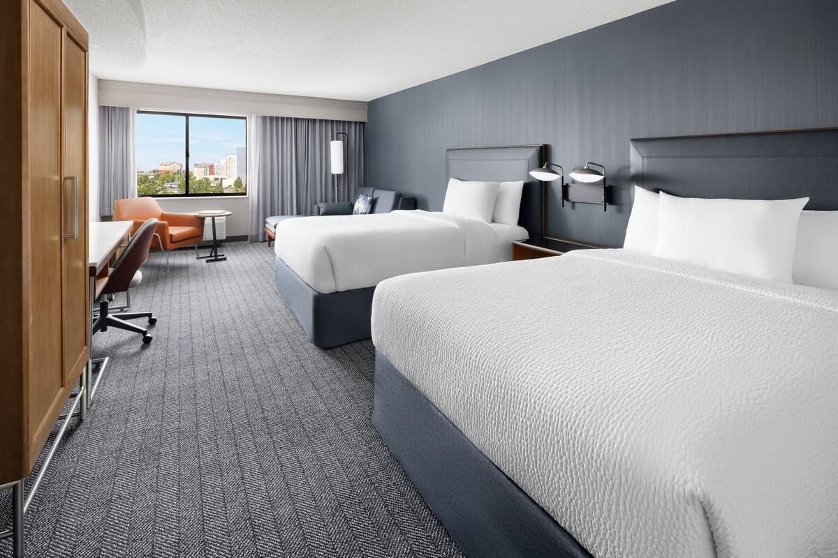 Ein Hotelzimmer mit zwei Betten, einem Schreibtisch, einem Stuhl und Blick auf die Stadt.