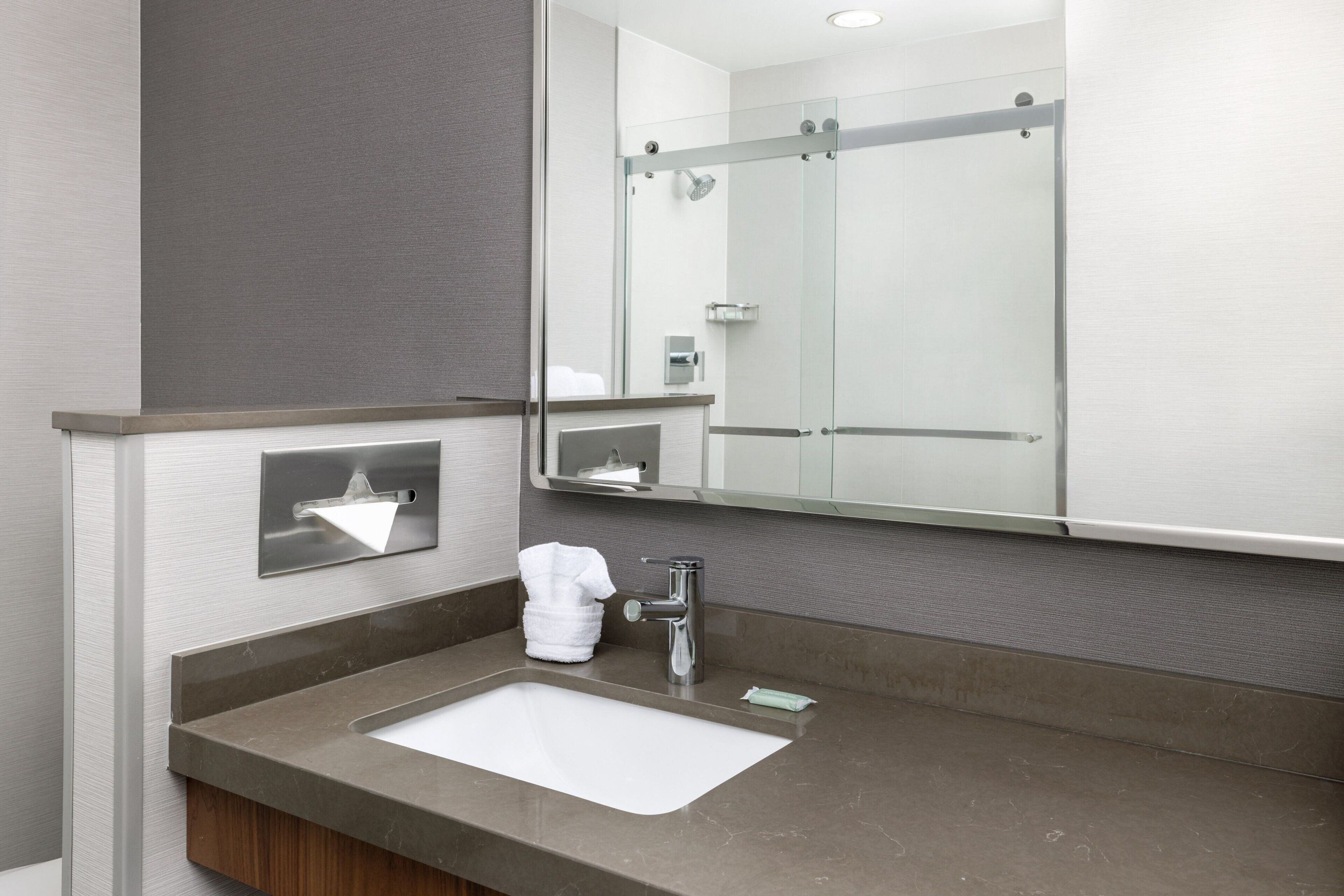 A modern bathroom with a large mirror, a sink, and a shower area.