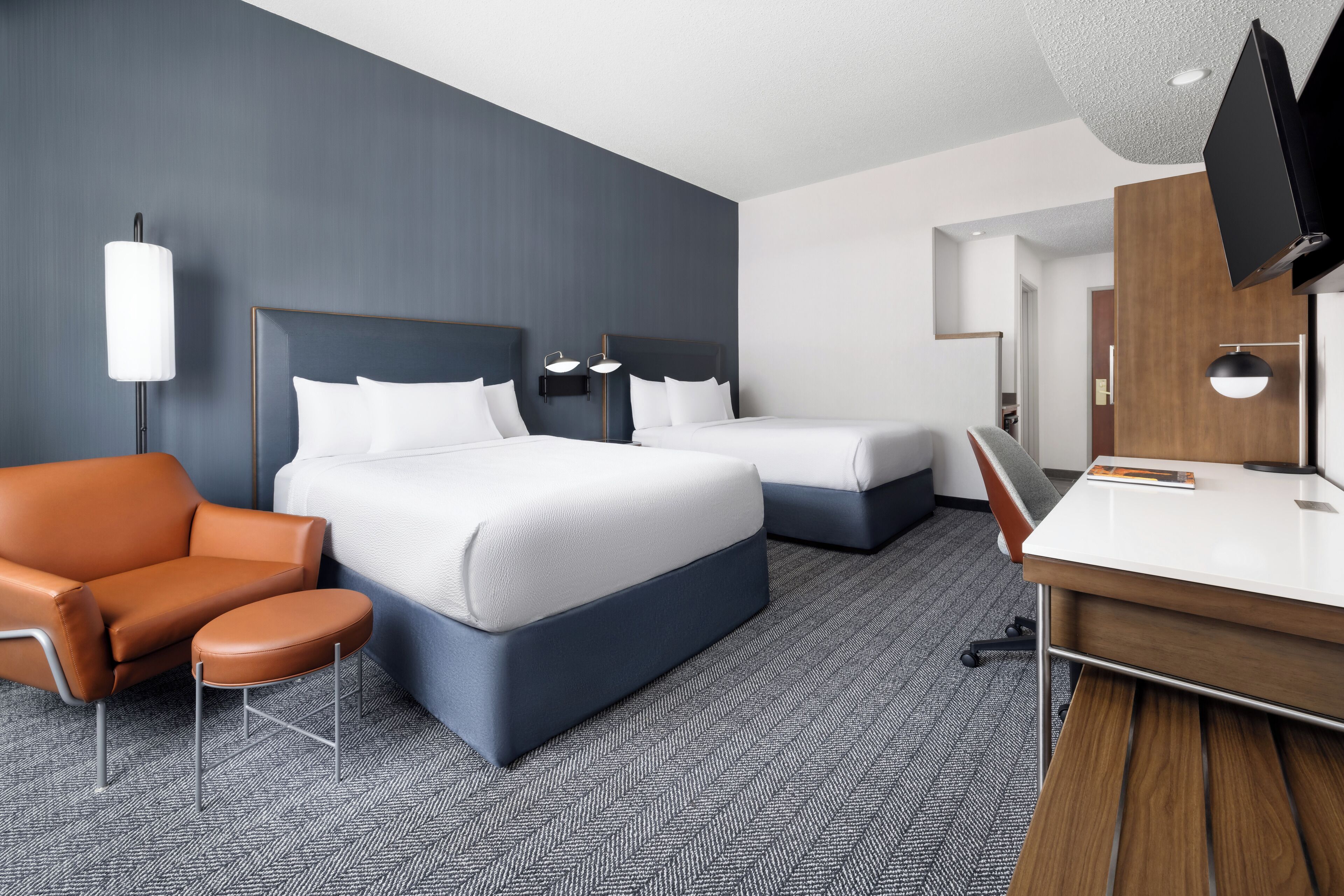 A hotel room with a large bed, a smaller bed, a desk, a chair, and a TV.