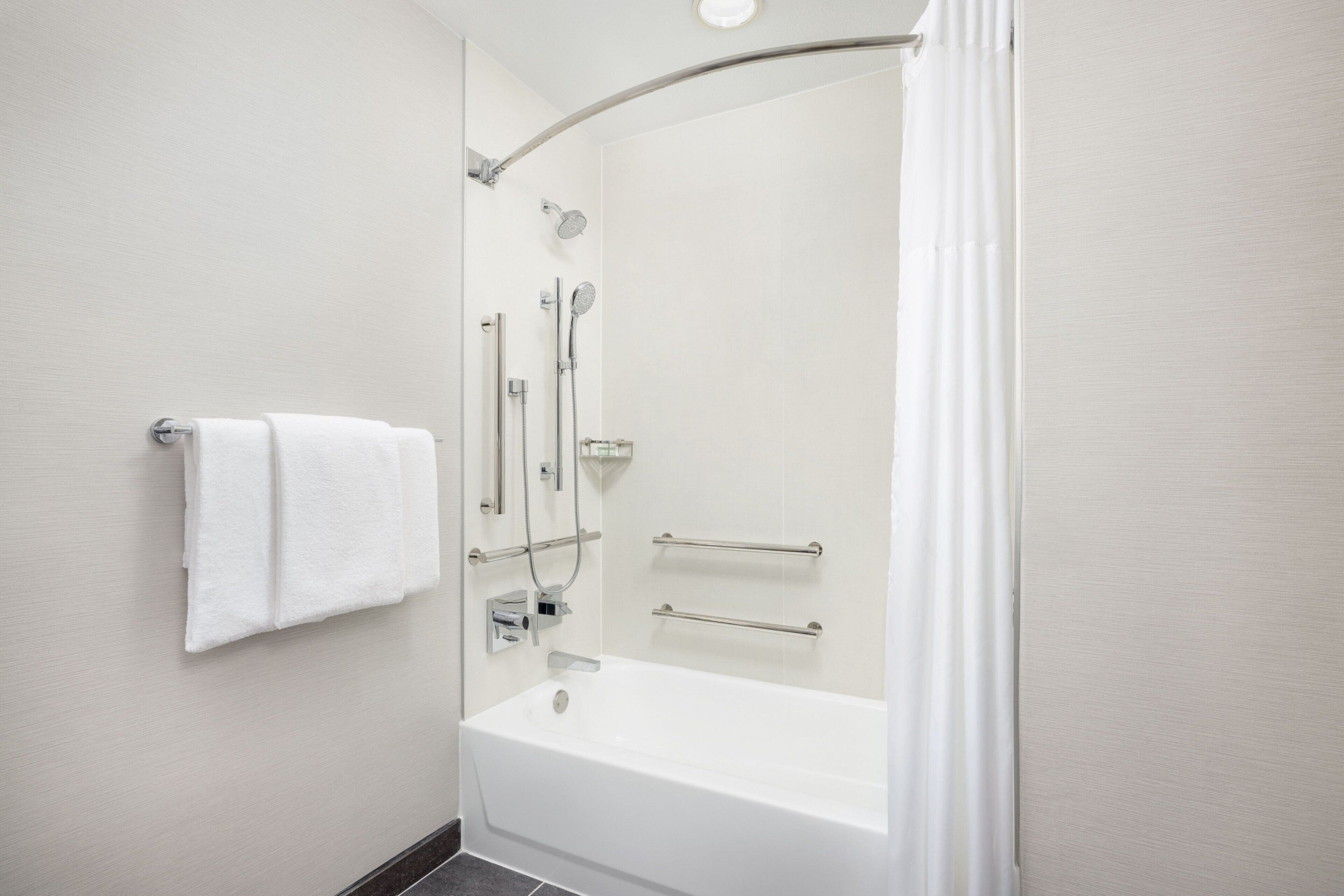 A modern bathroom with a bathtub, shower, and handrails.