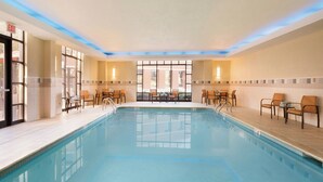 Una piscina interior con agua cristalina, rodeada de sillones de descanso y mesas, y amplias ventanas que dejan entrar luz natural.