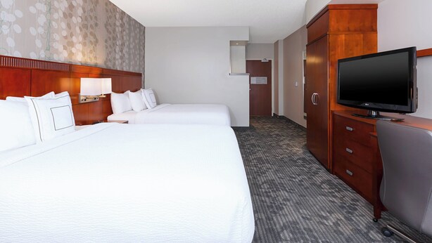 Habitación de hotel con dos camas, televisor, escritorio y armario.