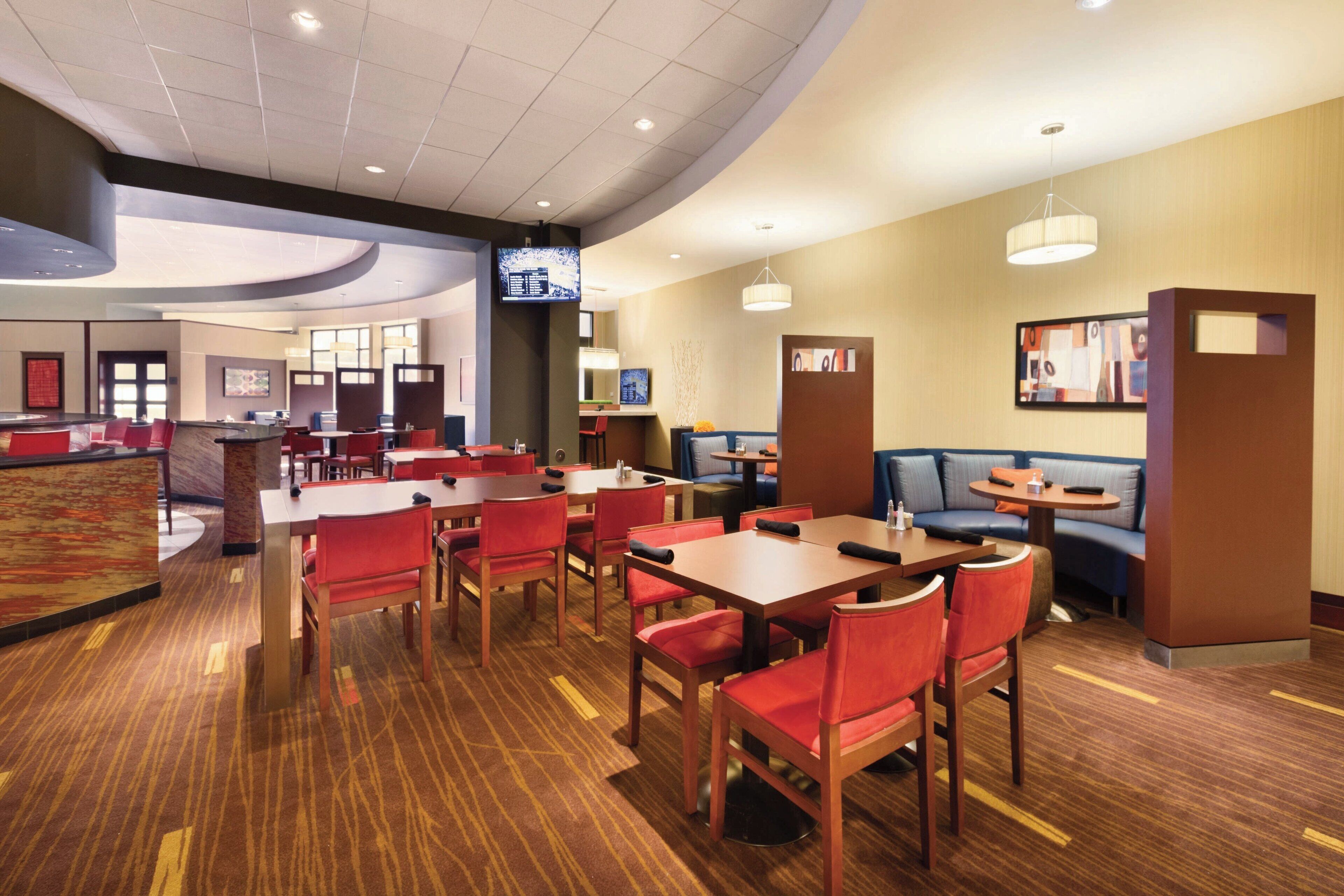 A hotel lobby with multiple seating areas, including tables and booths, and a reception desk.