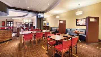 A hotel lobby with multiple seating areas, including tables and booths, and a reception desk.