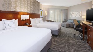 Habitación de hotel con dos camas, un escritorio, una silla, un televisor y un ventanal con cortinas.