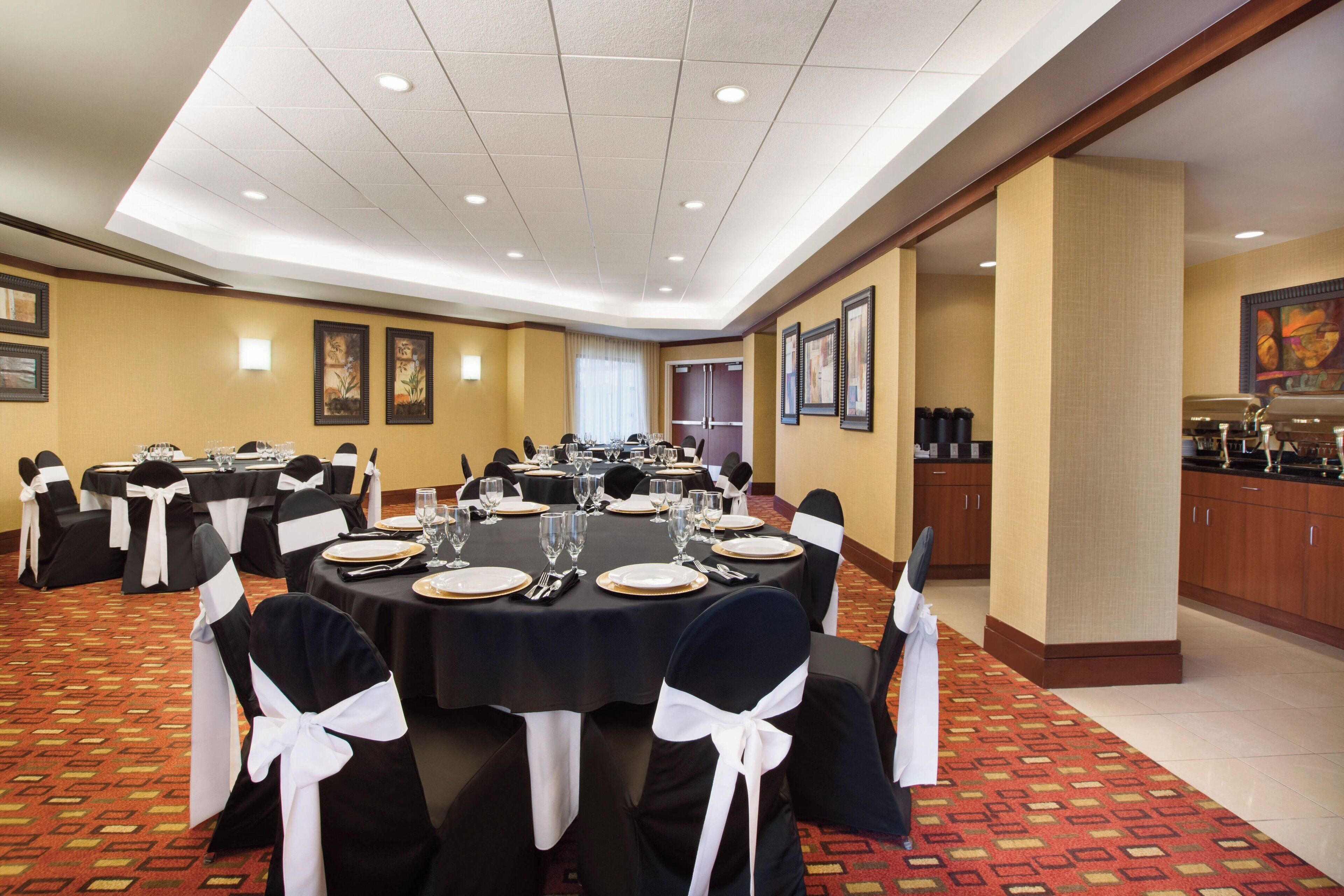 A conference room with round tables, black and white chairs, and a kitchen area in the background.