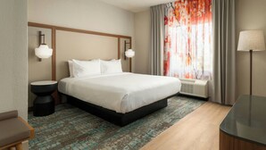 Une chambre d’hôtel avec un grand lit, deux tables de chevet, un bureau, une fenêtre avec des rideaux et une lampe fixée au mur.