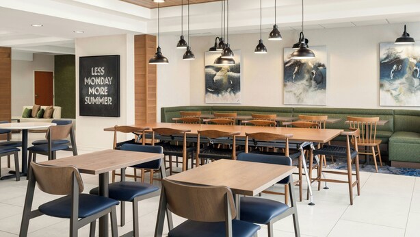 Un espace repas moderne avec des tables et des chaises en bois, des luminaires suspendus et des œuvres d’art accrochées aux murs.