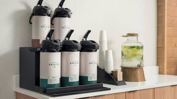 Una estación de bebidas con varios dispensadores, vasos desechables y una jarra grande de té helado.