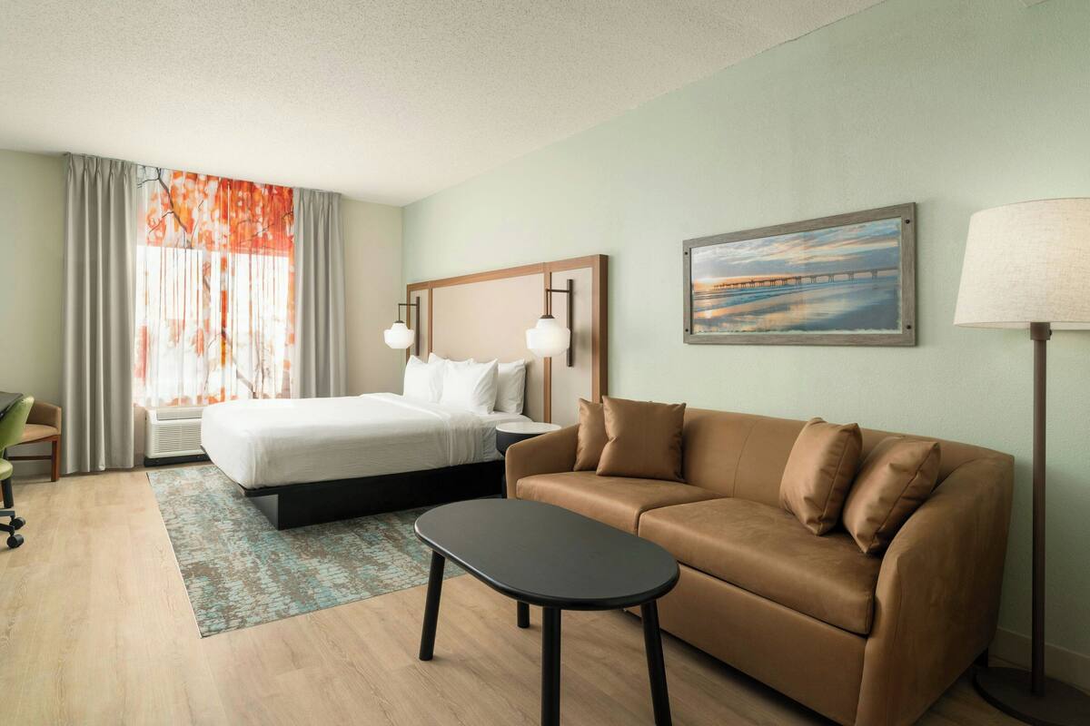 Una habitación de hotel con cama, sofá, una mesita, escritorio y lámpara.