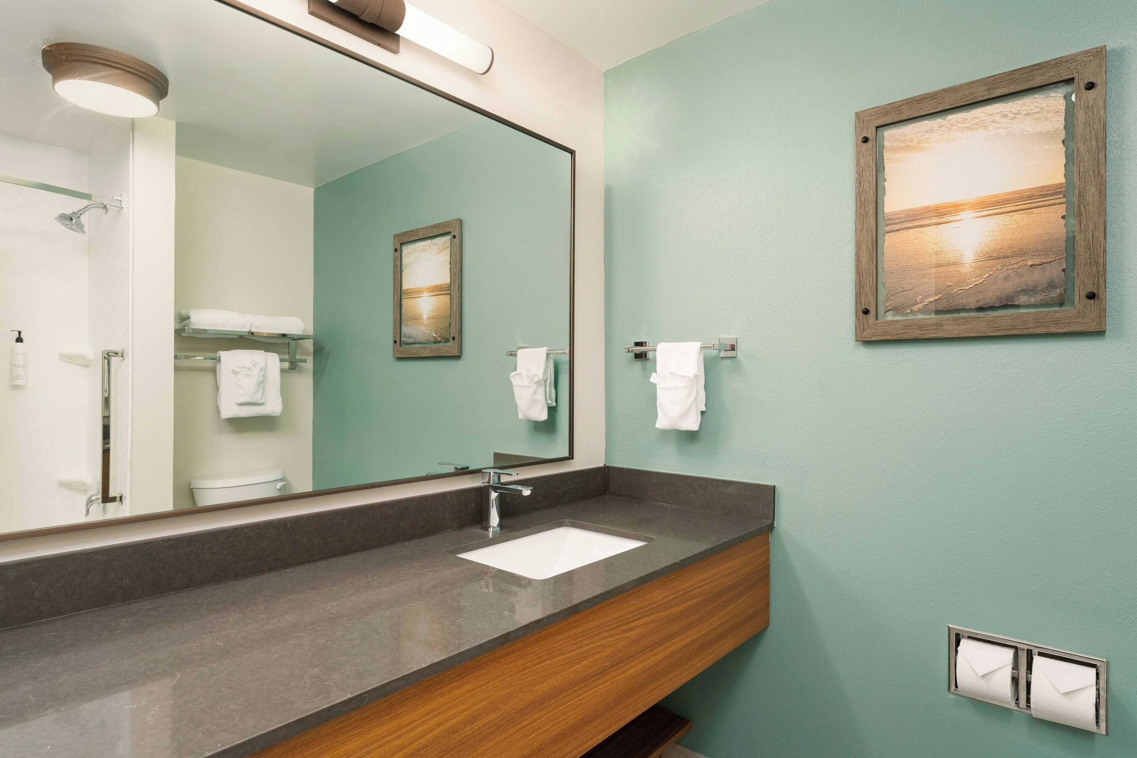 A bathroom with a large mirror, a sink, and a towel rack.