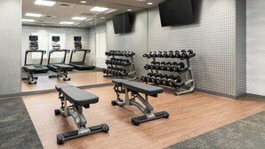 Une salle de sport équipée de tapis de course, d’haltères et de bancs.
