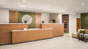 Un espace d’accueil comprenant un comptoir de réception en bois, un élément décoratif mural et un coin salon avec un canapé et deux petites tables.