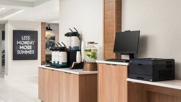 Una moderna reception con uno schermo piatto, una stampante Dell e un angolo caffè con bicchieri usa e getta e una macchina per il caffè.