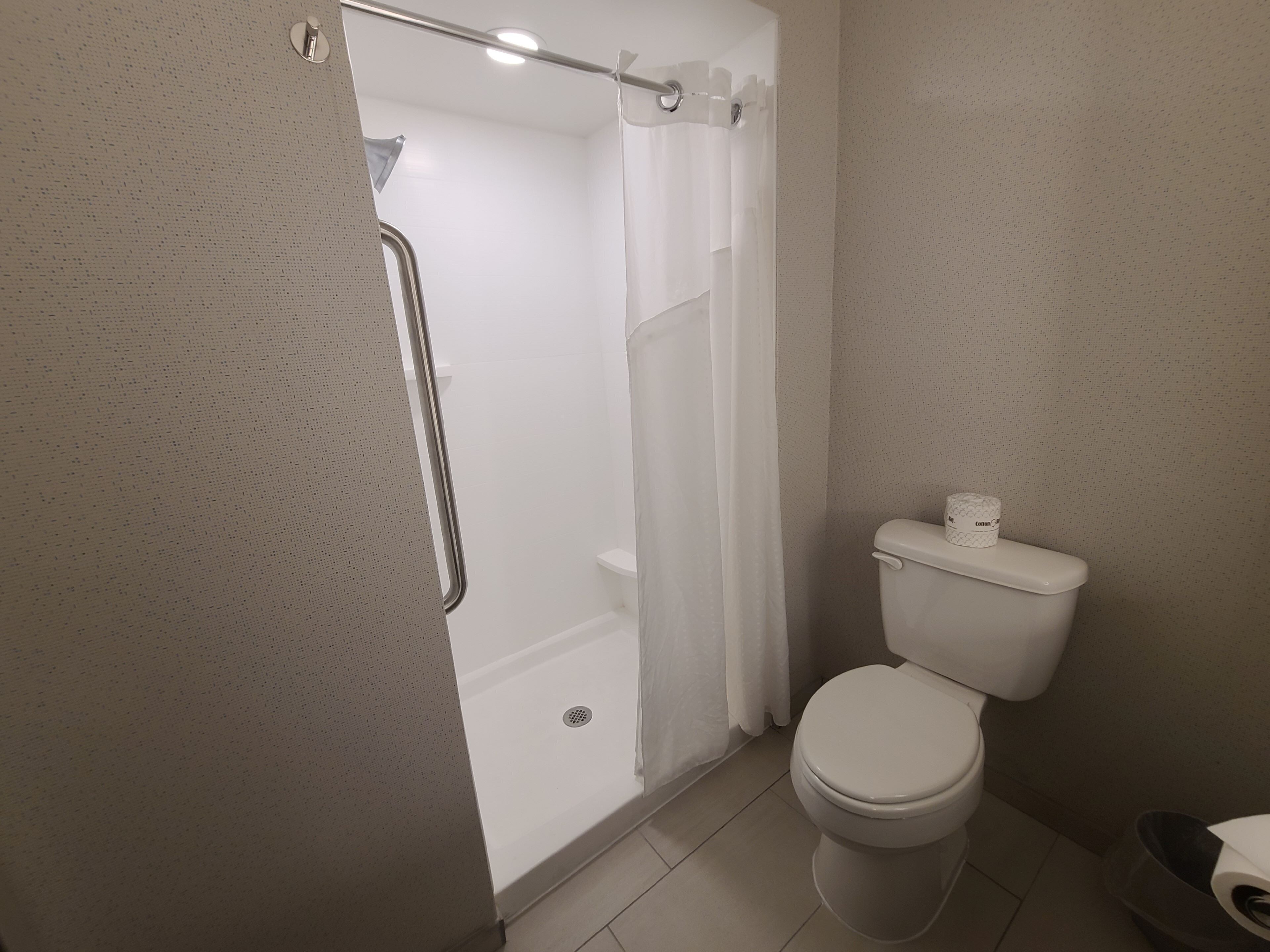 Un baño con inodoro, ducha con cortina y pared blanca.